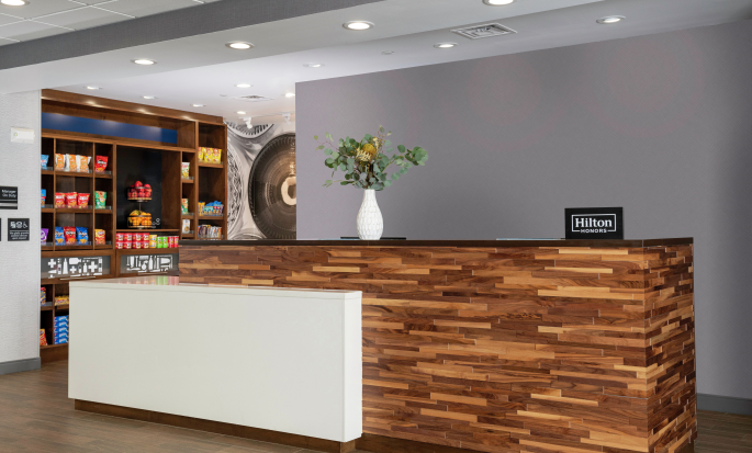 The front desk at a Hampton by Hilton. The desk is made of various colored wood with a warm gray backdrop.